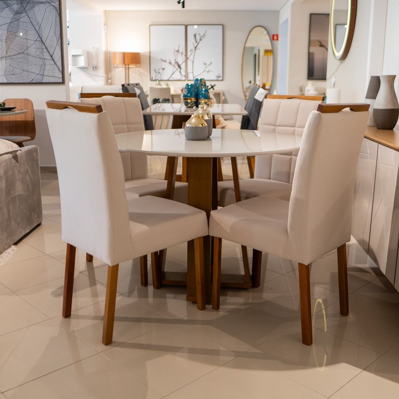 Mesa de jantar redonda Isabela com tampo off-white brilhante e base de madeira, cercada por quatro cadeiras de encosto alto estofadas em bege