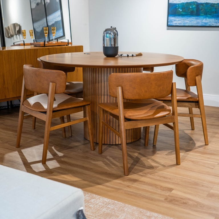 Mesa de jantar redonda Select com tampo em lâmina de madeira e base cilíndrica ripada, cercada por cadeiras de couro caramelo