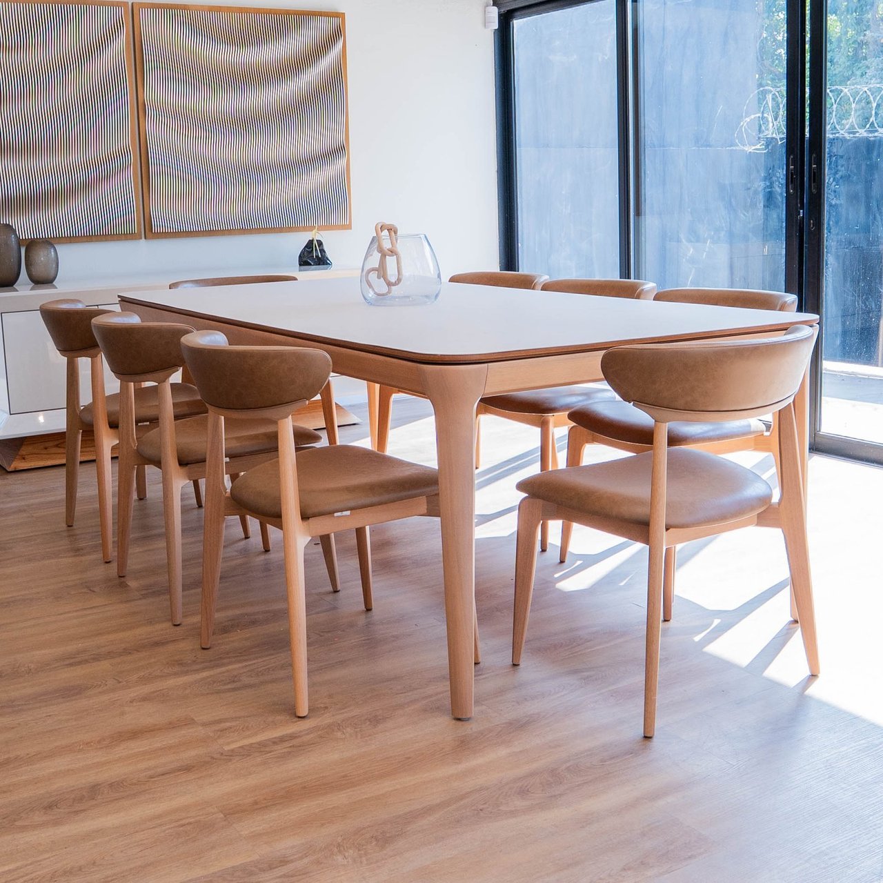 Mesa de jantar Theo com tampo claro de borda em madeira e pernas orgânicas, cercada por cadeiras de madeira com assento caramelo