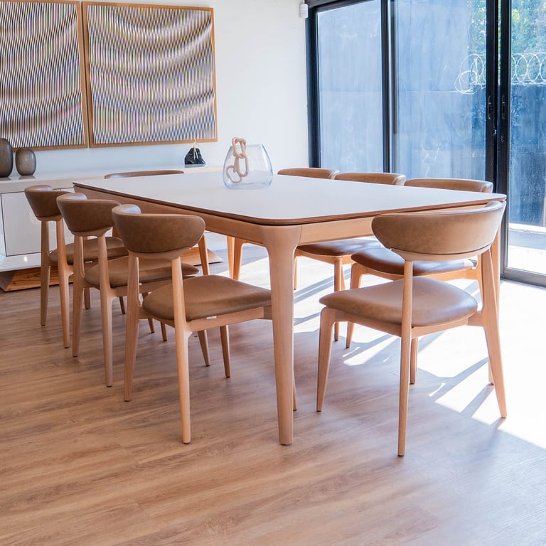Mesa de jantar Theo com tampo claro de borda em madeira e pernas orgânicas, cercada por cadeiras de madeira com assento caramelo