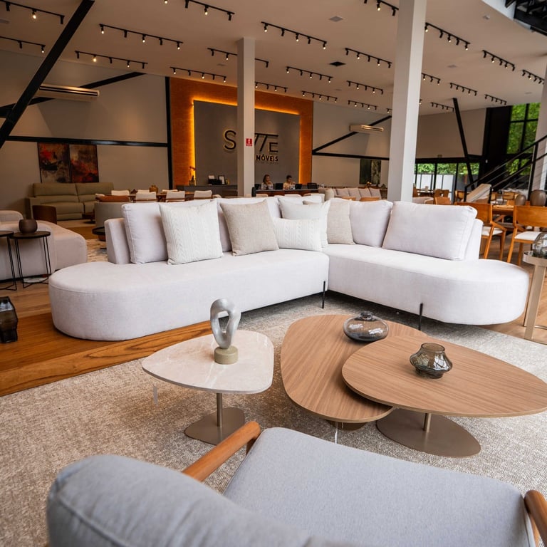 Sofá Modular LV007 curvo em tecido off-white, com chaise arredondada e pés palito metálicos, em showroom