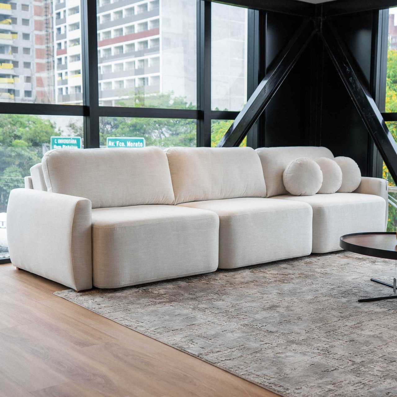 Sofá Noah modular em tecido off-white, com encosto baixo, almofadas soltas e almofadas-rolo, em showroom