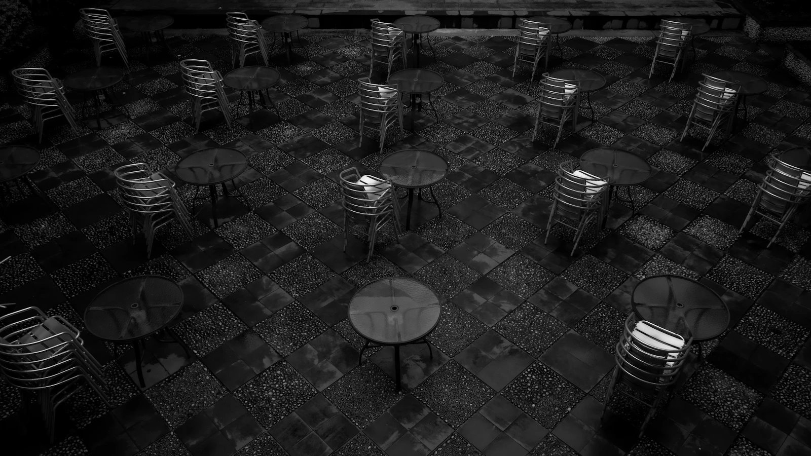 Stacked metal chairs beside round tables on a tiled outdoor patio.