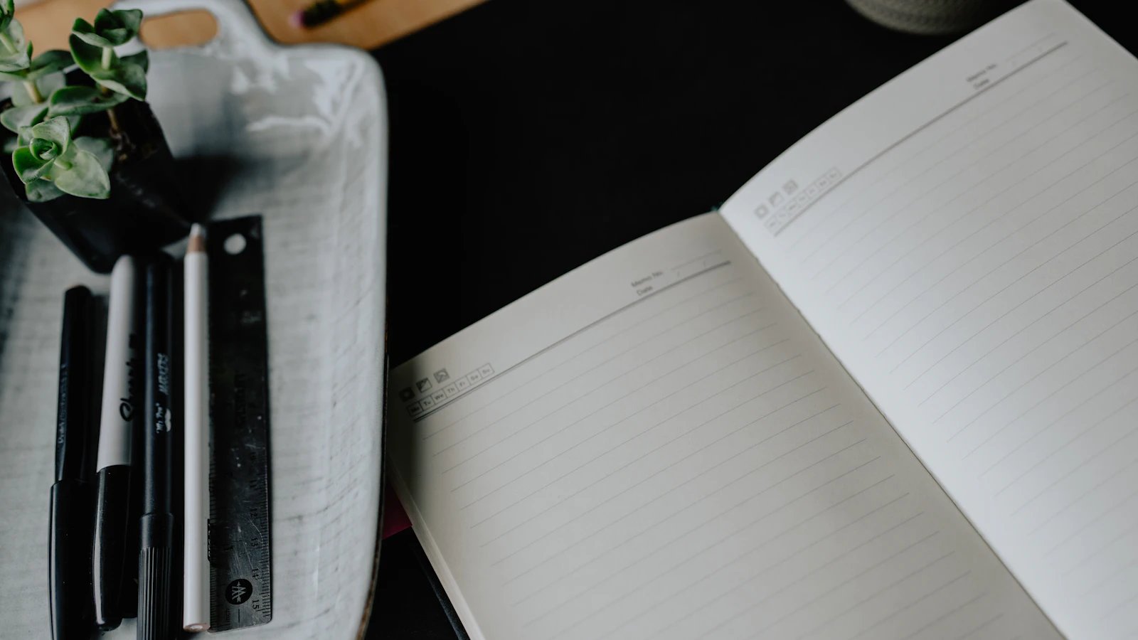 An open notebook with facing lined pages and pens beside it.