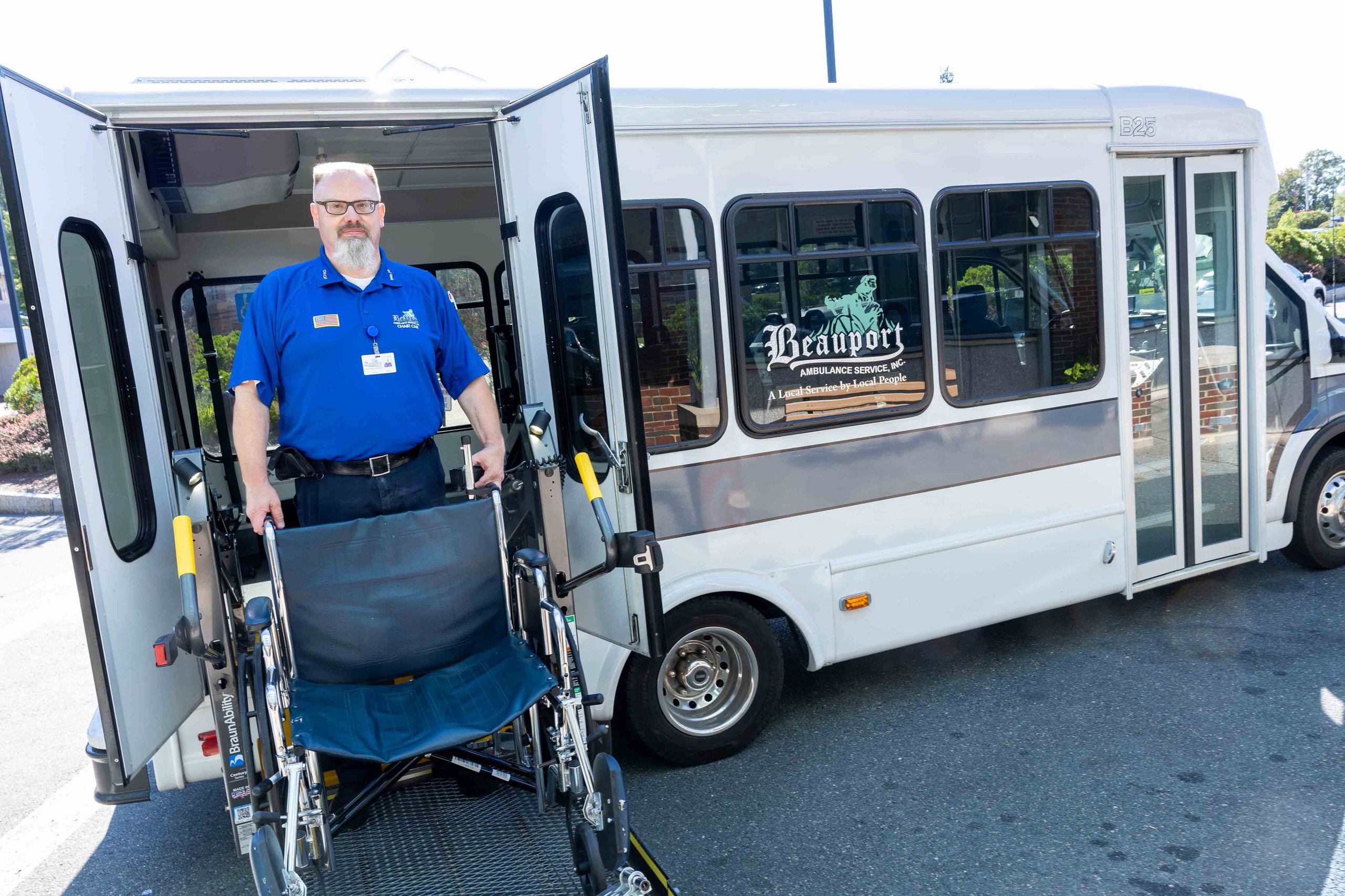 A staff member holds a wheelchair next to a company bus.