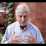 Michael Dukakis in a screenshot from one of the videos, standing in front of a red brick wall.