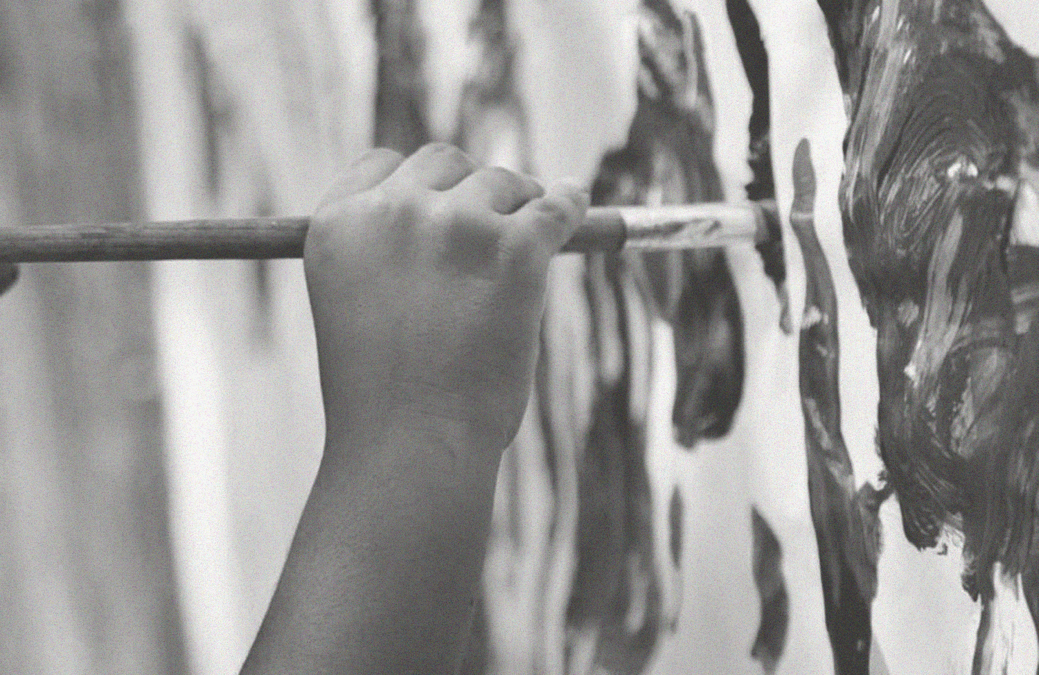 A hand holding a brush painting on a piece of paper.