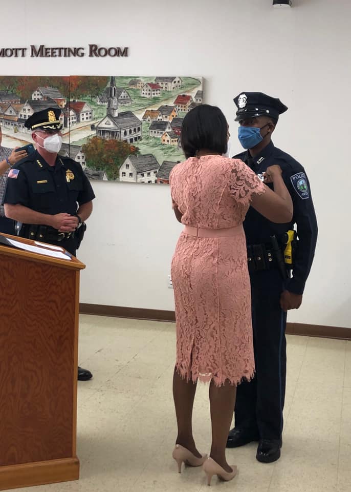 Avon Police Chief Jeffrey Bukunt, left, looks on as Officer Hans Guillaume’s mother, Marguerite Guillaume, pins his badge on his chest during a swearing in ceremony on Thursday, June 25. (Photo courtesy Avon Police Department)