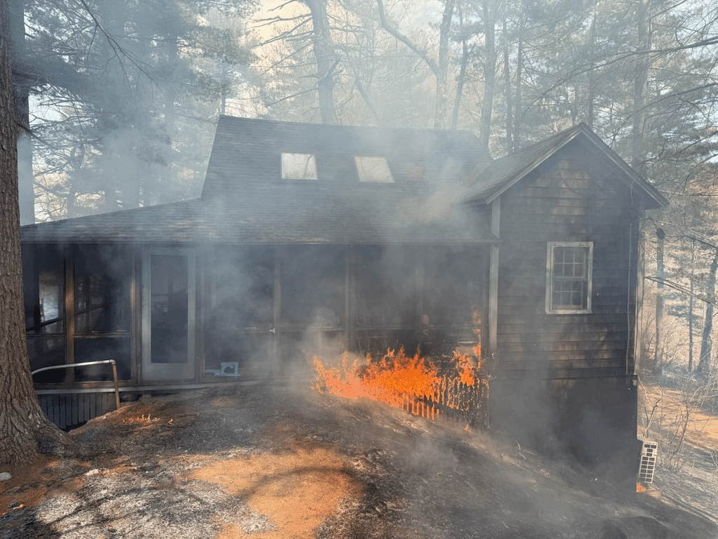 A significant brush fire spread to an unoccupied, seasonal log cabin in the area of Lowell and Old Dunstable roads on Tuesday afternoon. Firefighters from Groton and several mutual aid communities were eventually able to extinguish the fire. (Photo Courtesy Groton Fire Department)