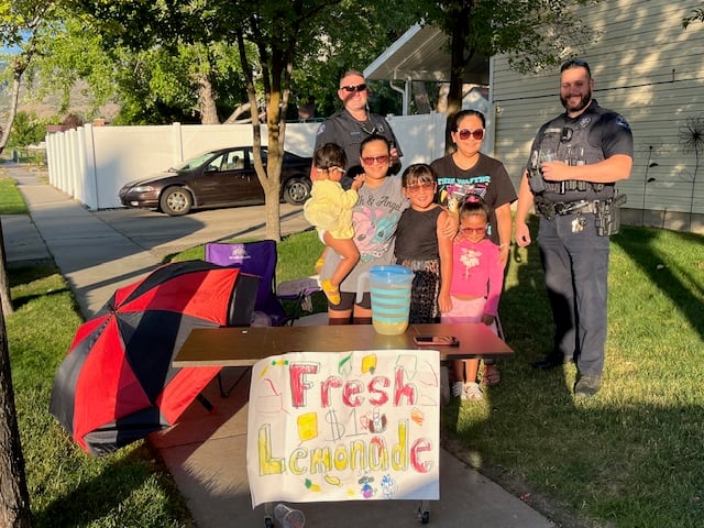 "Smiles, sips, and service — Harrisville officers join young entrepreneurs for a refreshing community moment."