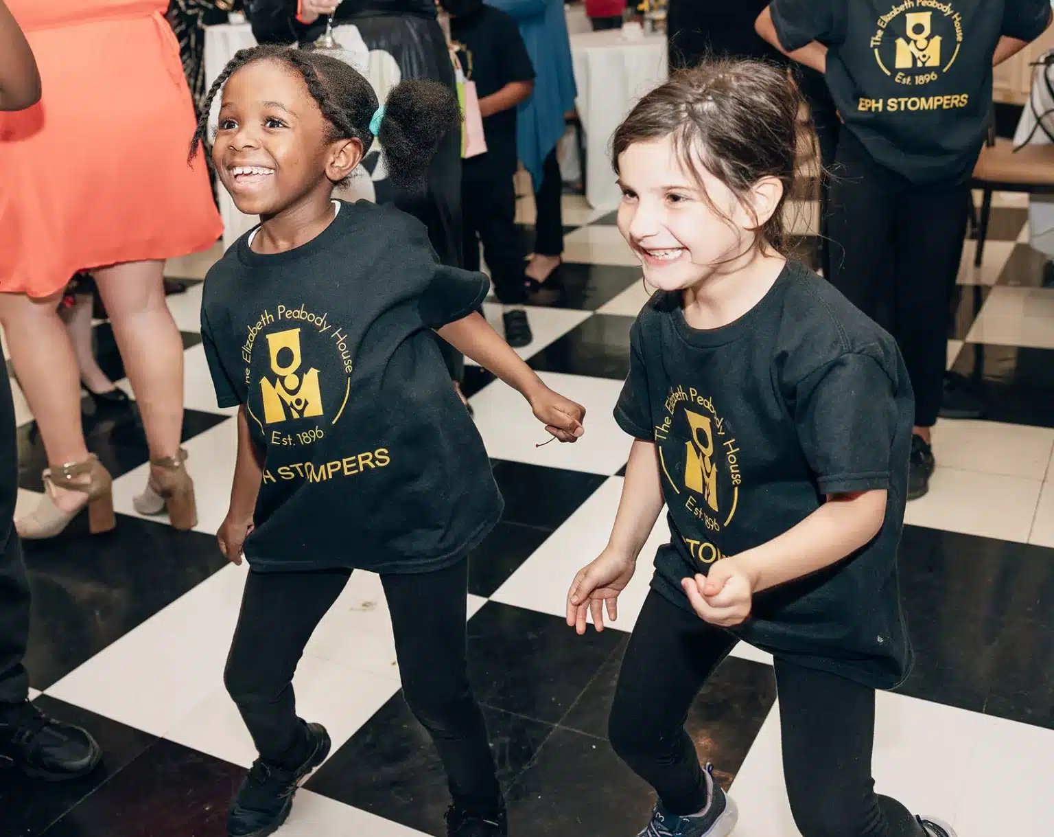 Two young girls wearing EPH black shirts dance.