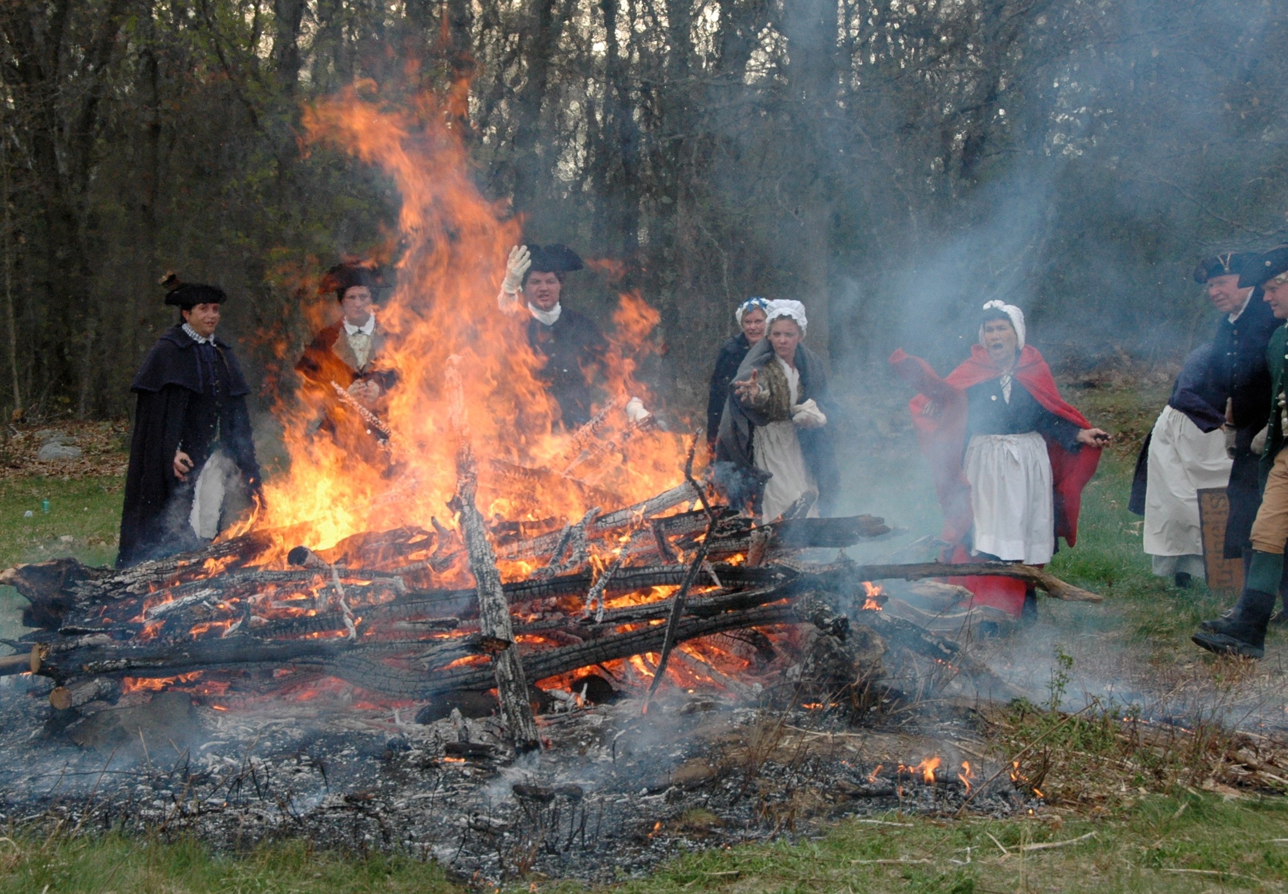 Boston Tea party reenactors throwing tea into a large fire.