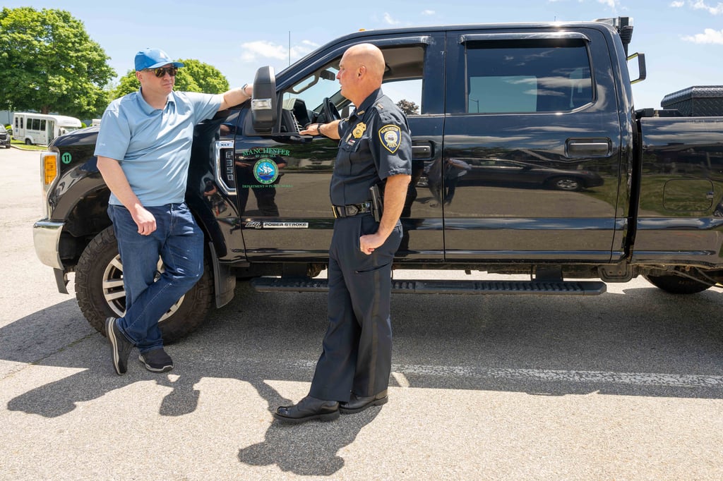 Police officer talks to a man standing next to a large black truck.