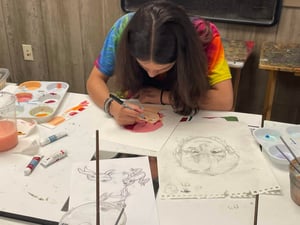A teen girl wearing a tie dye shirt draws with colored pencils.