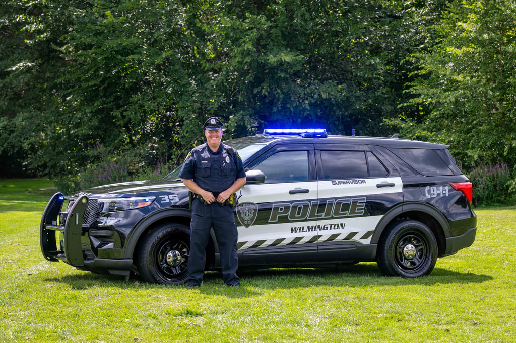 Male police officer standing in front of a cruiser.