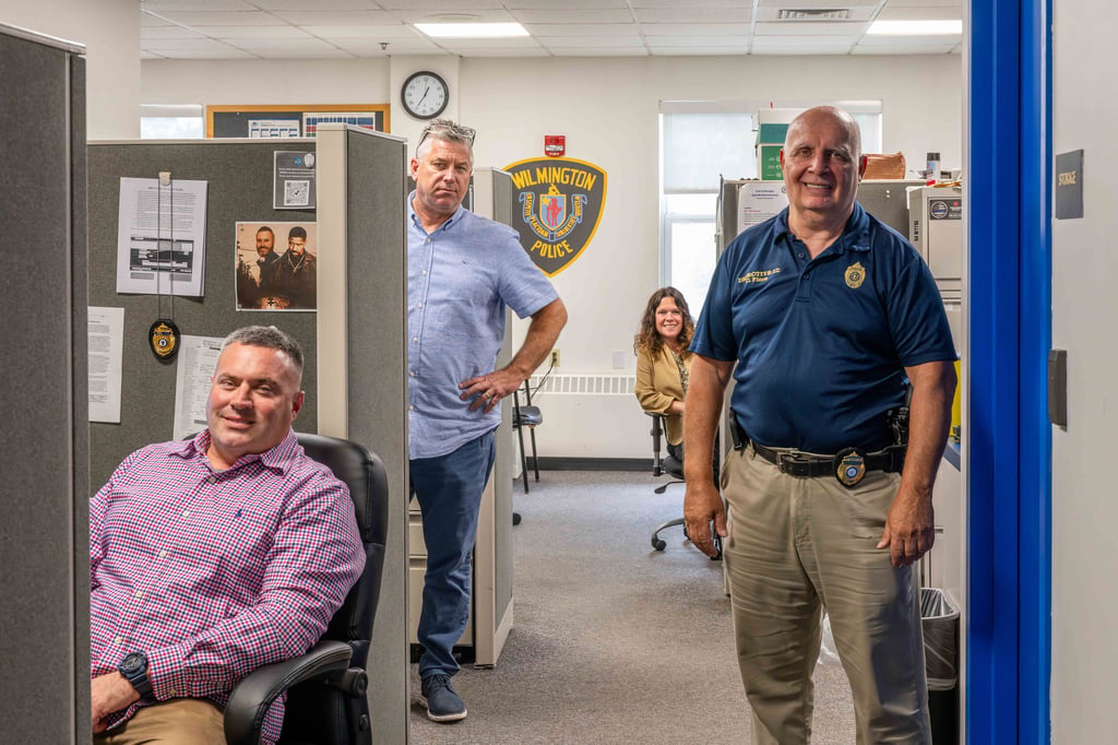 Four members of the Wilmington Police Department stand near their desks in the headquarters office.