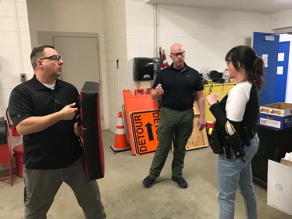 Two male police officers training a woman on physical combat.