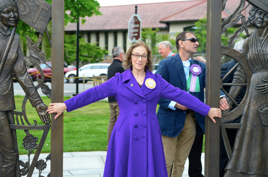 A woman in a purple coat stands in the arch of a new statue to commemorate women in Lexington's history.
