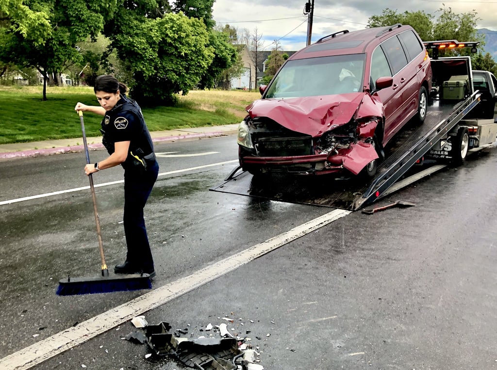 A female police officer sweeps up debris after a crash.