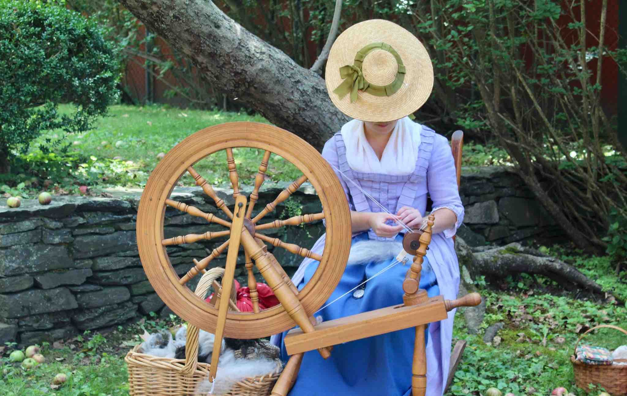 A woman wearing historical garb spins yarn.