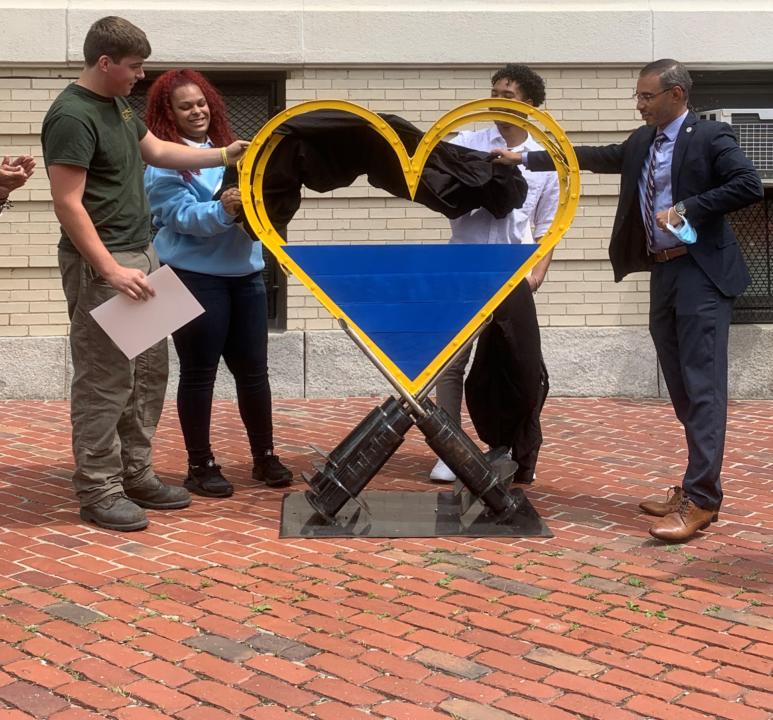 From left, Greater Lawrence Technical School students Brady Valliere, Orlendi Hernandez, Carlos Burgos and Lawrence Mayor Kendrys Vasquez remove a covering to reveal the COVID-19 metal sculpture designed by about 10 Metal Fabrication students.
