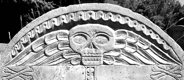 Closeup of an intricately carved skull on a gravestone.
