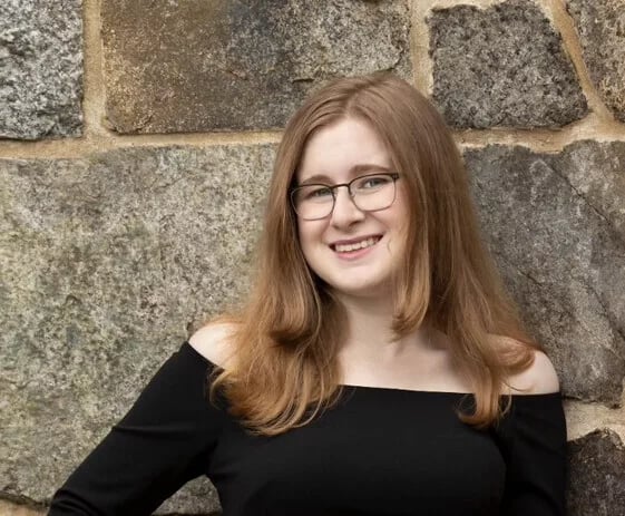 Student wearing glasses and black dress stands against rock wall
