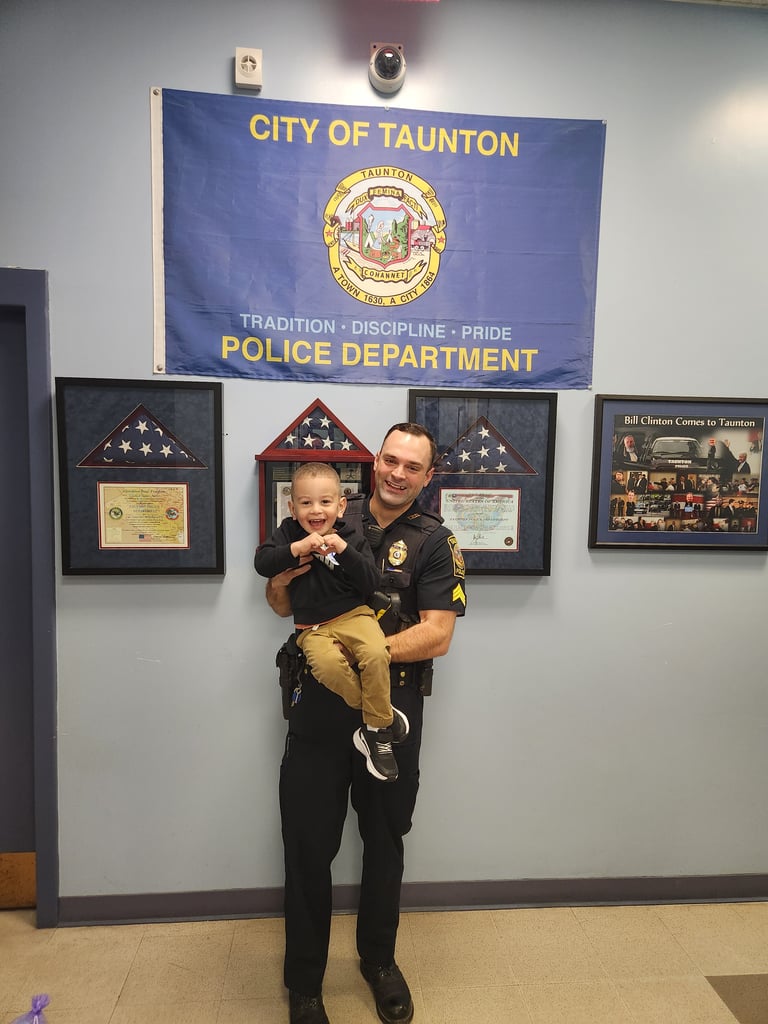 Taunton Police Sgt. Matthew Laranjo holds 2-year-old Joseph Teodoro while reuniting for the first time since Sgt. Laranjo helped to save Joseph's life when he was choking on food at daycare earlier this month. Joseph is making a heart with his hands. (Photo courtesy Taunton Police Department)