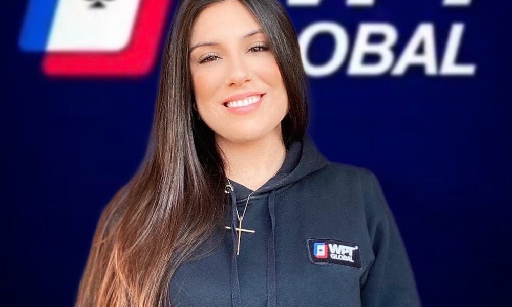 Andressa Lincoln wearing a WPT® Global hoodie smiling in front of a blue WPT® Global logo backdrop.