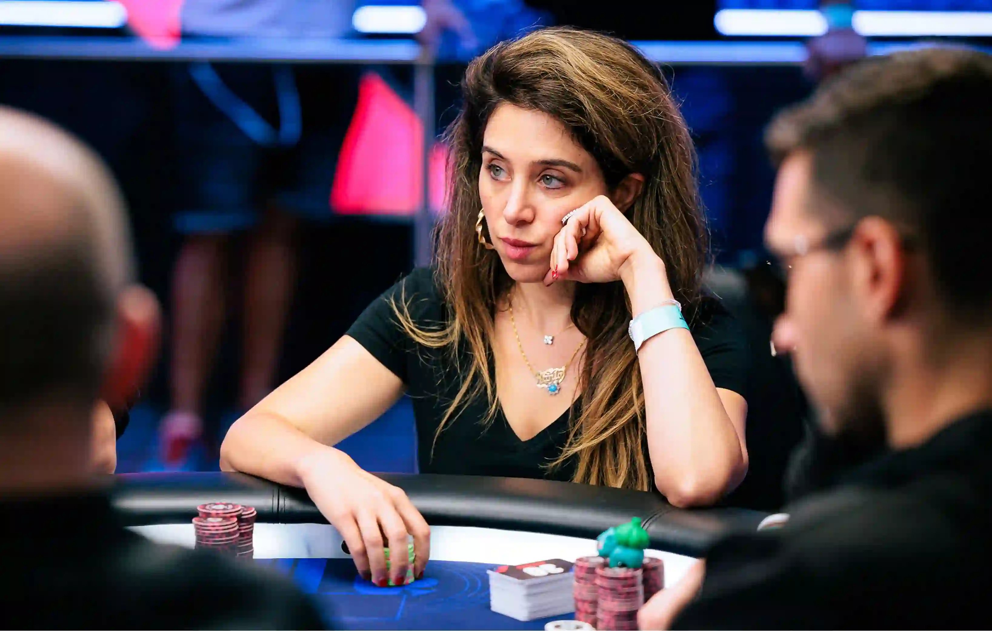 Rania Nasreddine rests her hand on her face while studying the action at a poker table with chip stacks nearby