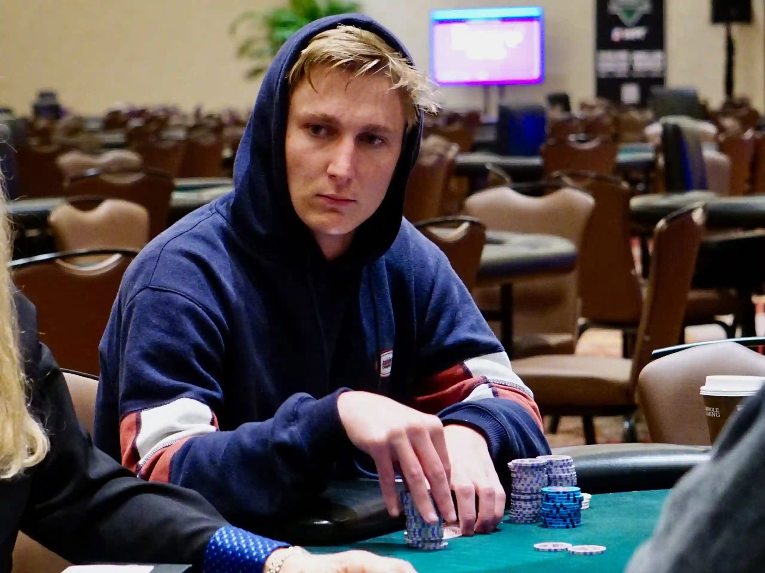 Connor Rash in a dark hoodie staring forward with chip stacks in front of him at a WPT® event.
