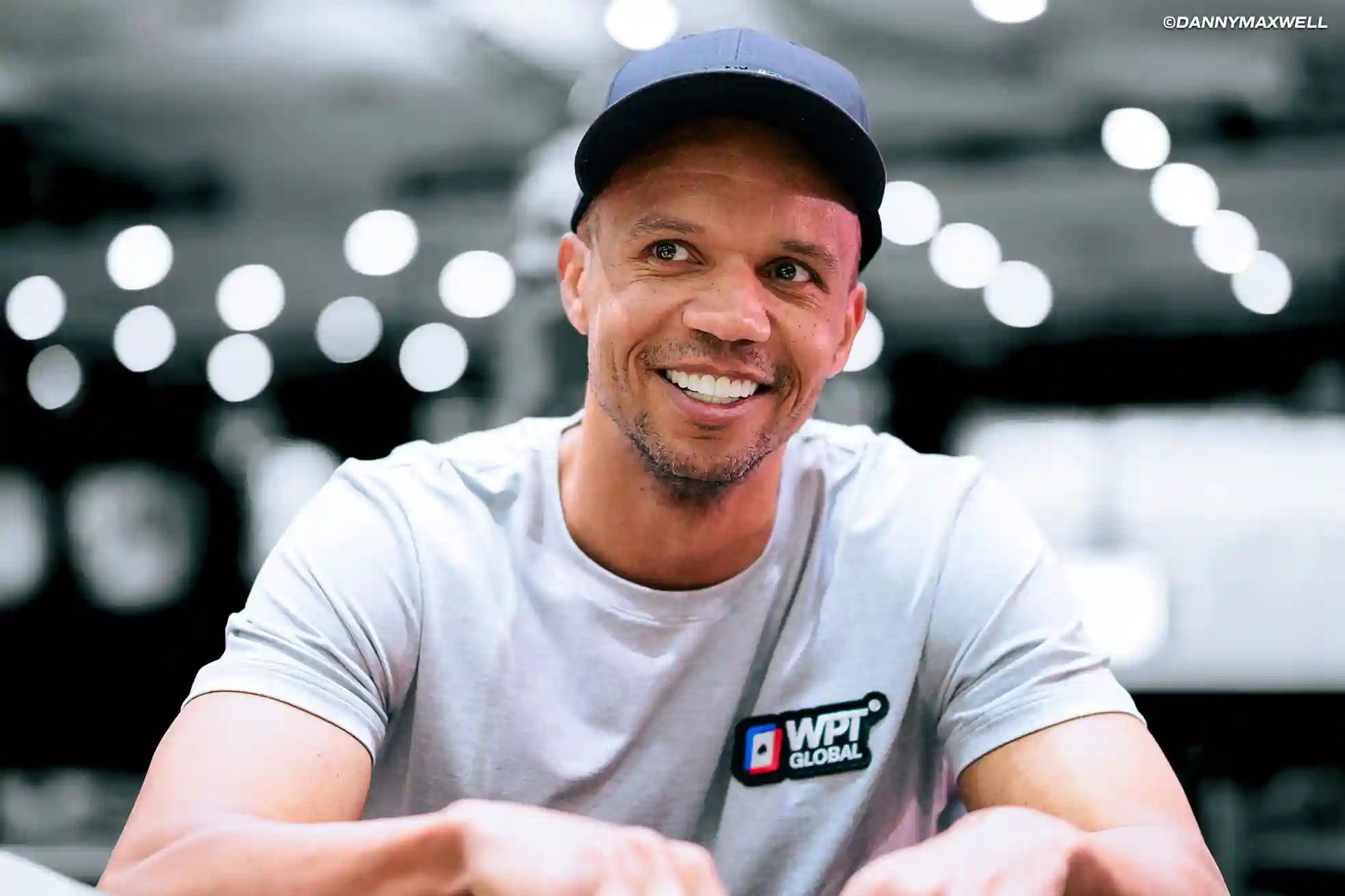 Phil Ivey in a WPT® Global T-shirt at a casino table with soft lights in the background.