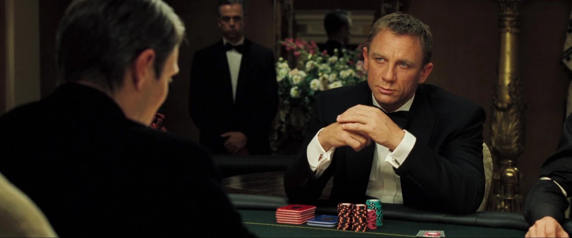 Daniel Craig as James Bond sits at a casino table with poker chips stacked in front of him during a high-stakes hand in Casino Royale.