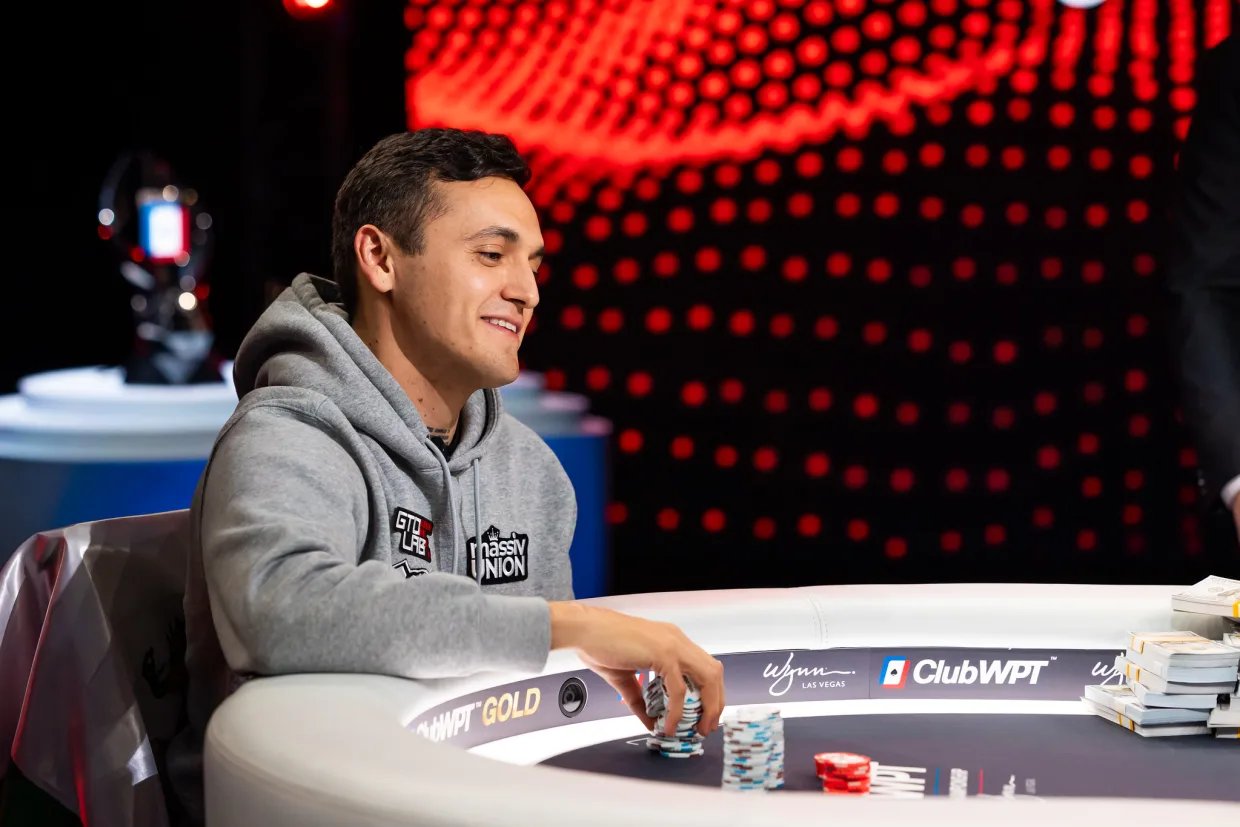 Smiling poker player in grey hoodie stacks chips at ClubWPT final table beside prize money.
