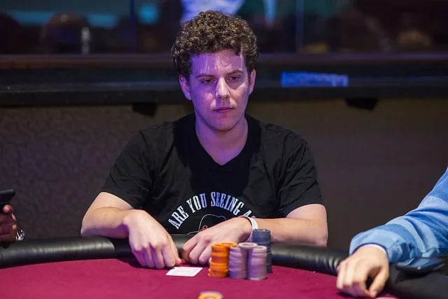 Ari Engel in a black T-shirt sits at a casino table with several stacks of chips, looking serious as he waits for the action.
