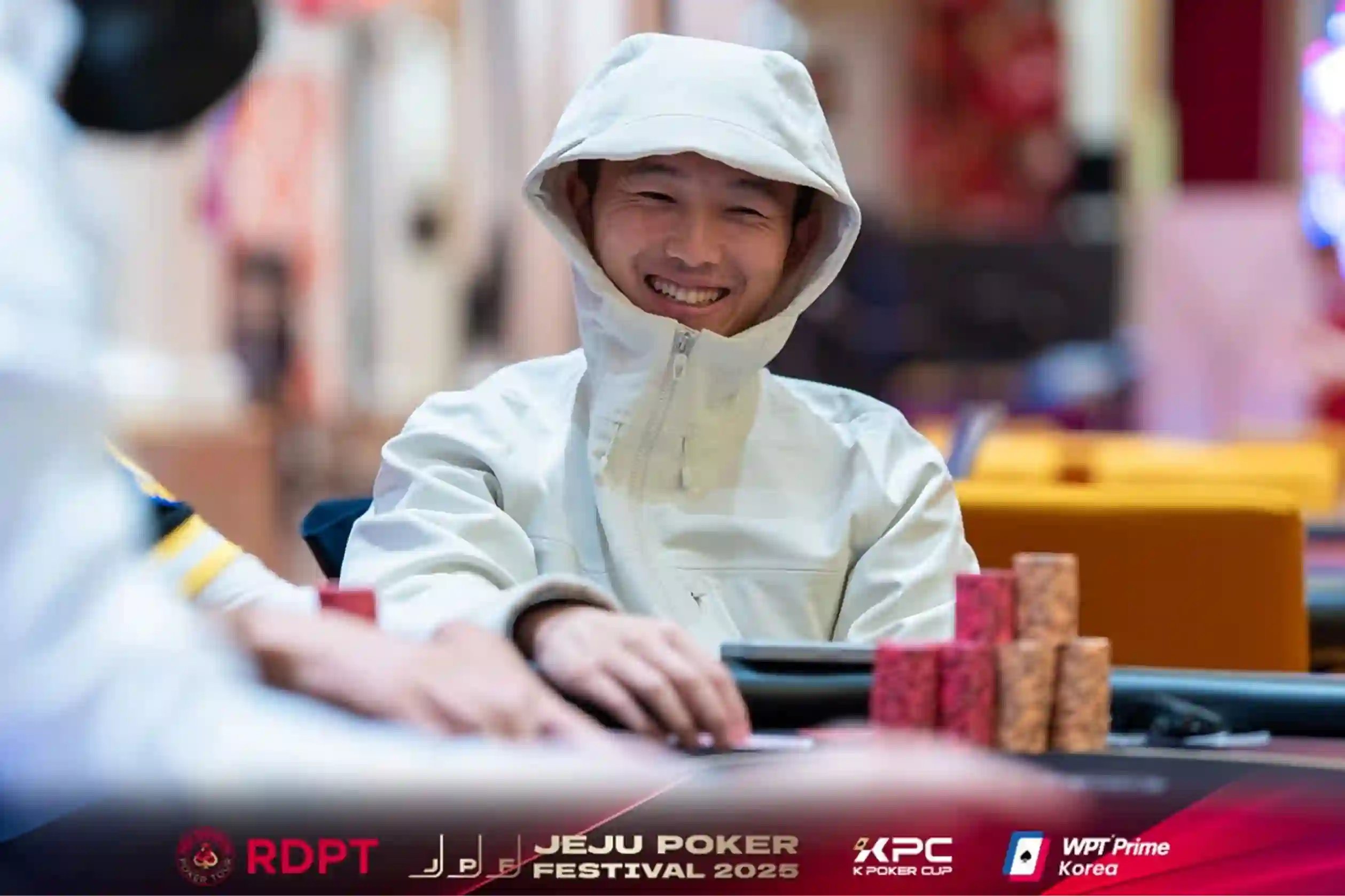Zengxiang Chen smiling in a light hooded jacket with a tall stack of chips during the Jeju Poker Festival at WPT® Prime Korea.