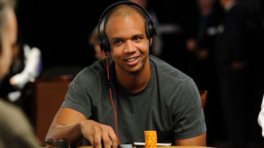 Phil Ivey smiling at the poker table while wearing headphones, with stacks of chips in front of him during live play.