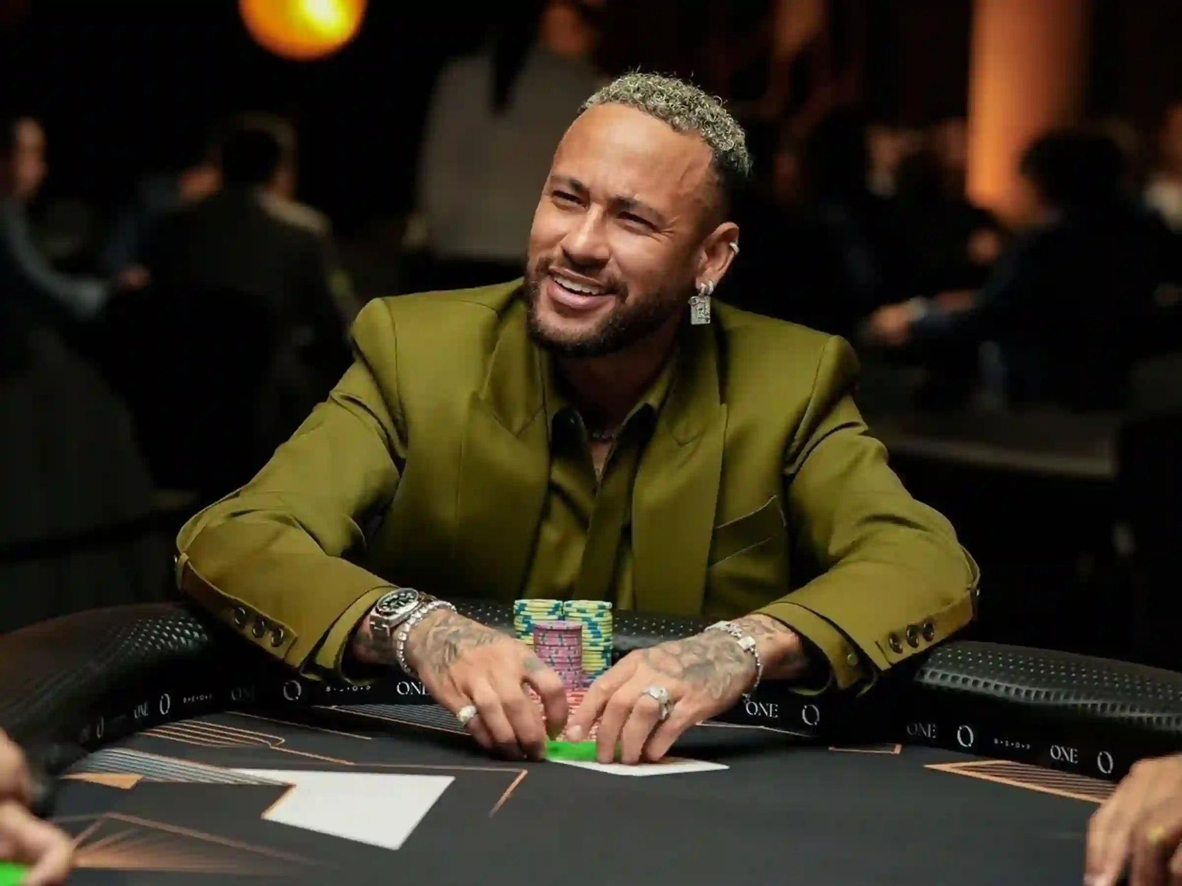 Smiling football star in a green blazer stacking poker chips at a high-stakes table.