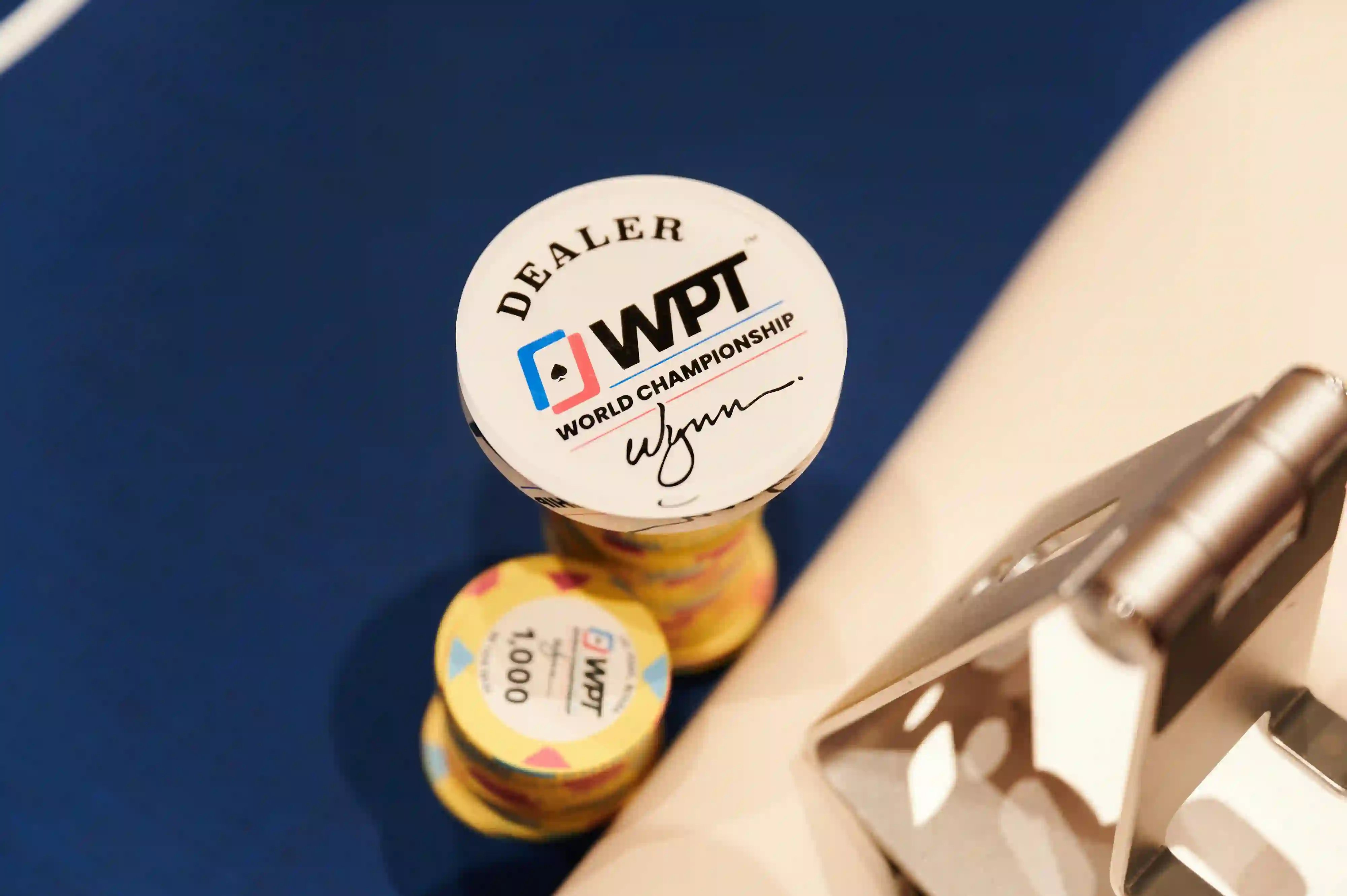 WPT® World Championship dealer button stacked on colorful tournament chips on blue felt.