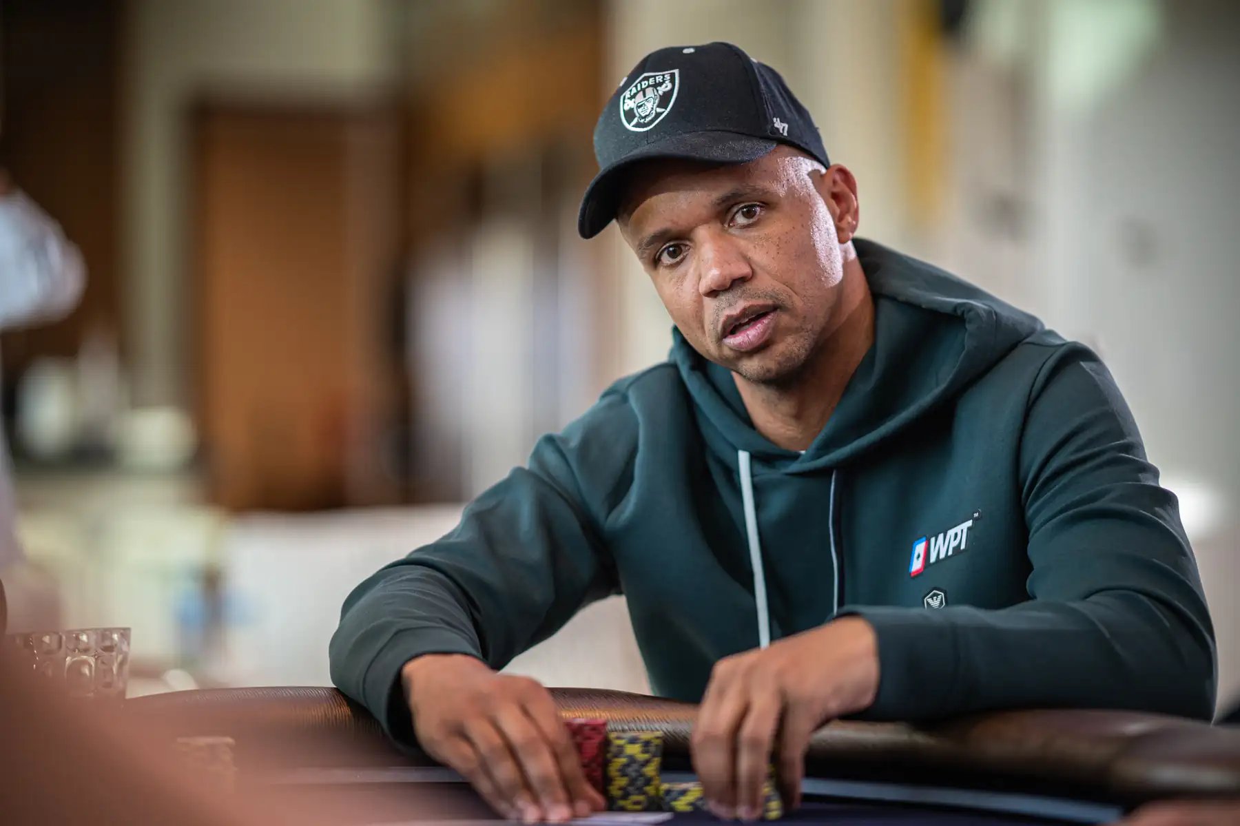 WPT®-branded hoodie wearing poker player in a cap stacking chips at a live table