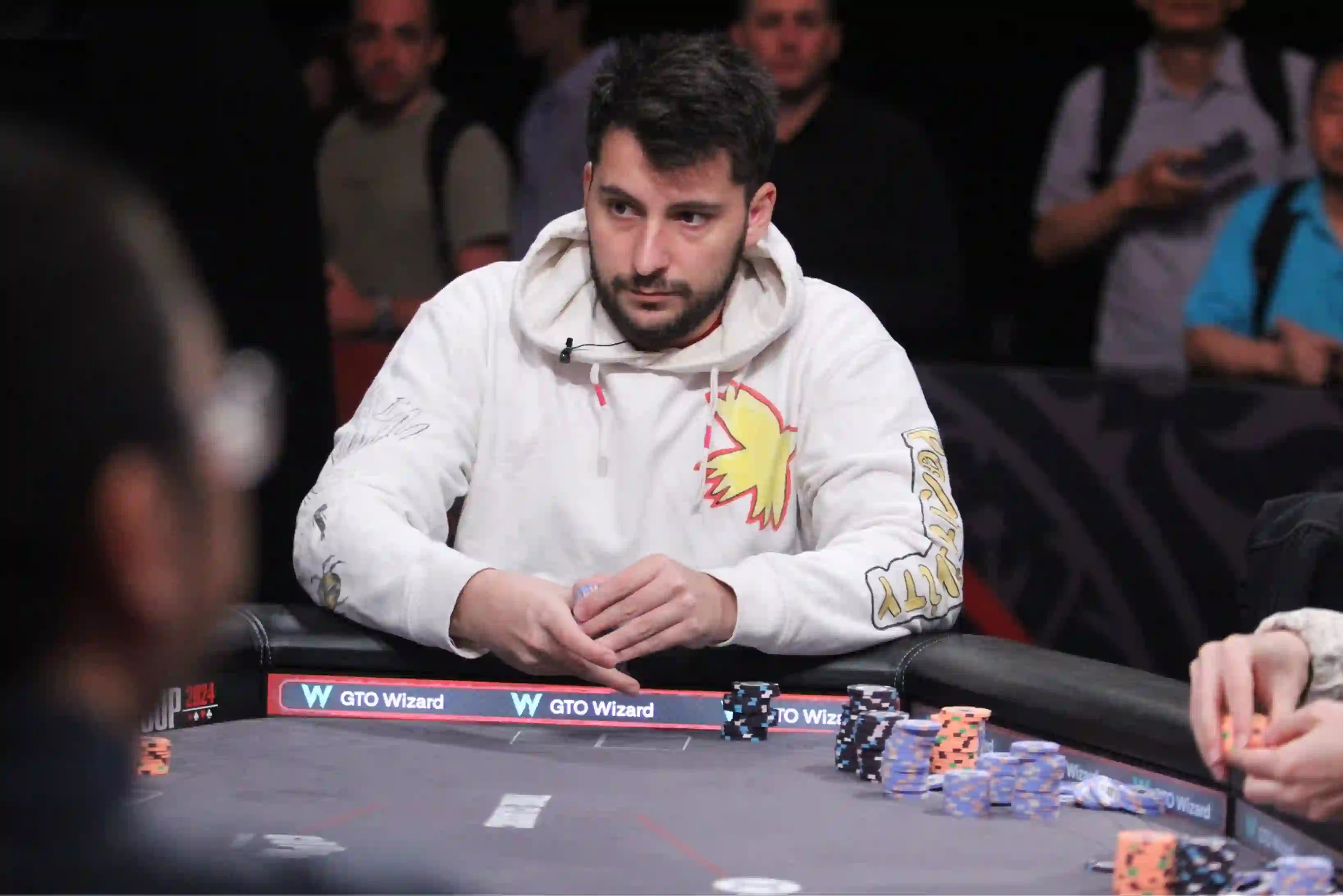 Boris Angelov sits at a poker table in a white hoodie, preparing to act with several stacks of chips in front of him