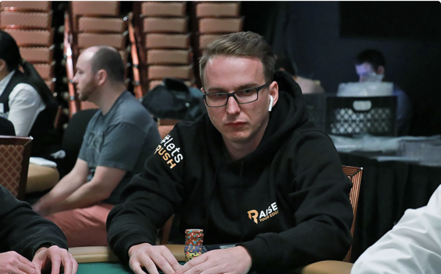 Benjamin Rolle wearing a black hoodie sits at the table stacking chips during a live event.