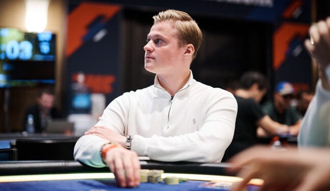 Casimir Seire in a white shirt looking to the side while seated at a live tournament table.