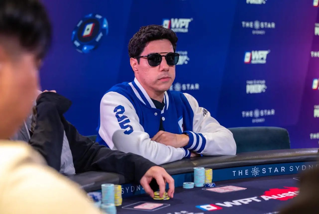 Sergio Barros plays a WPT® Australia event wearing a blue varsity jacket, working a growing chip stack.