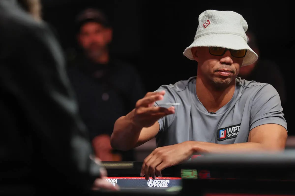 Phil Ivey wearing a WPT Global shirt and bucket hat focuses during a live poker tournament, holding a chip mid-hand.