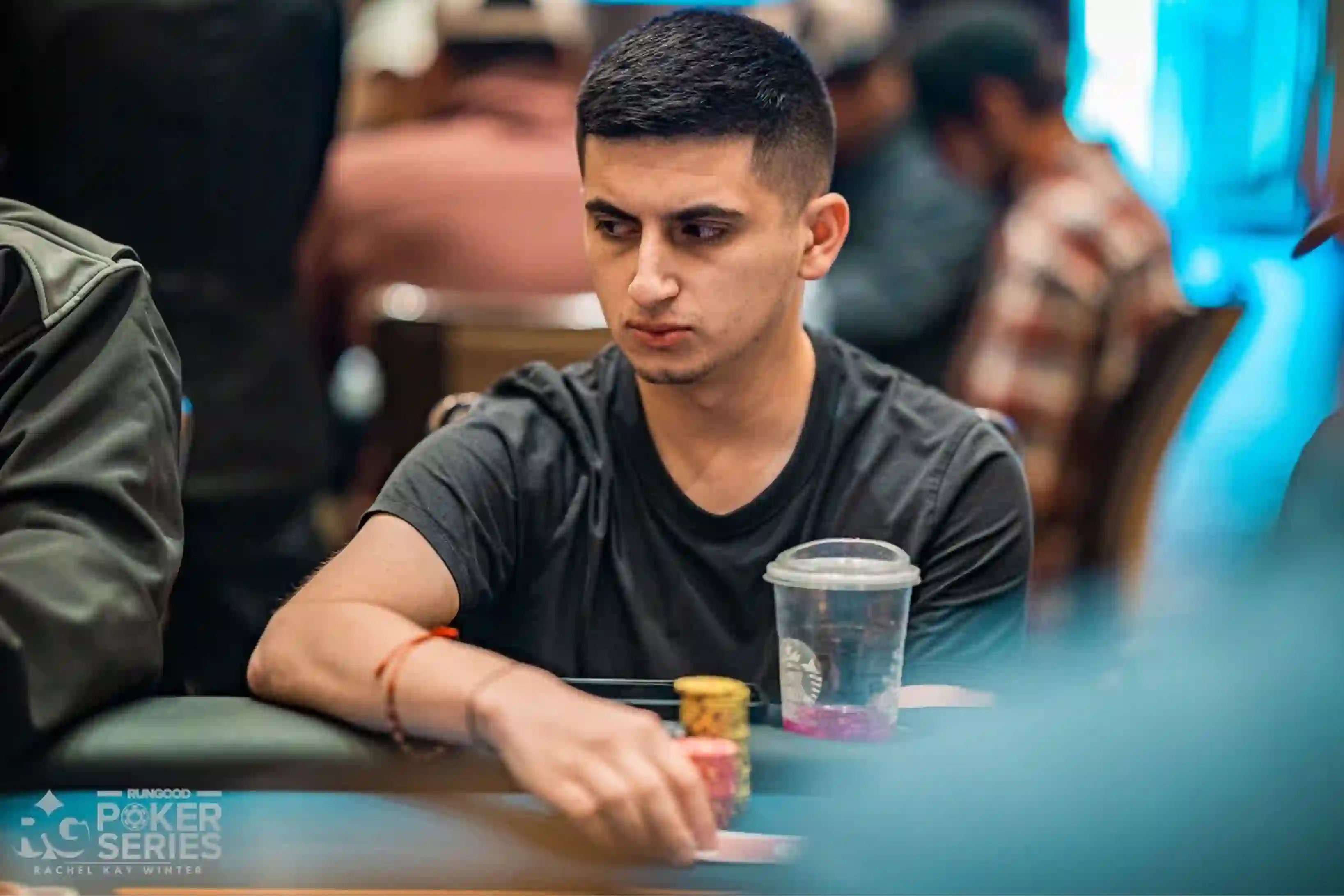 Noel Rodriguez focuses on the action while seated at a tournament table with chips and a drink in front of him.