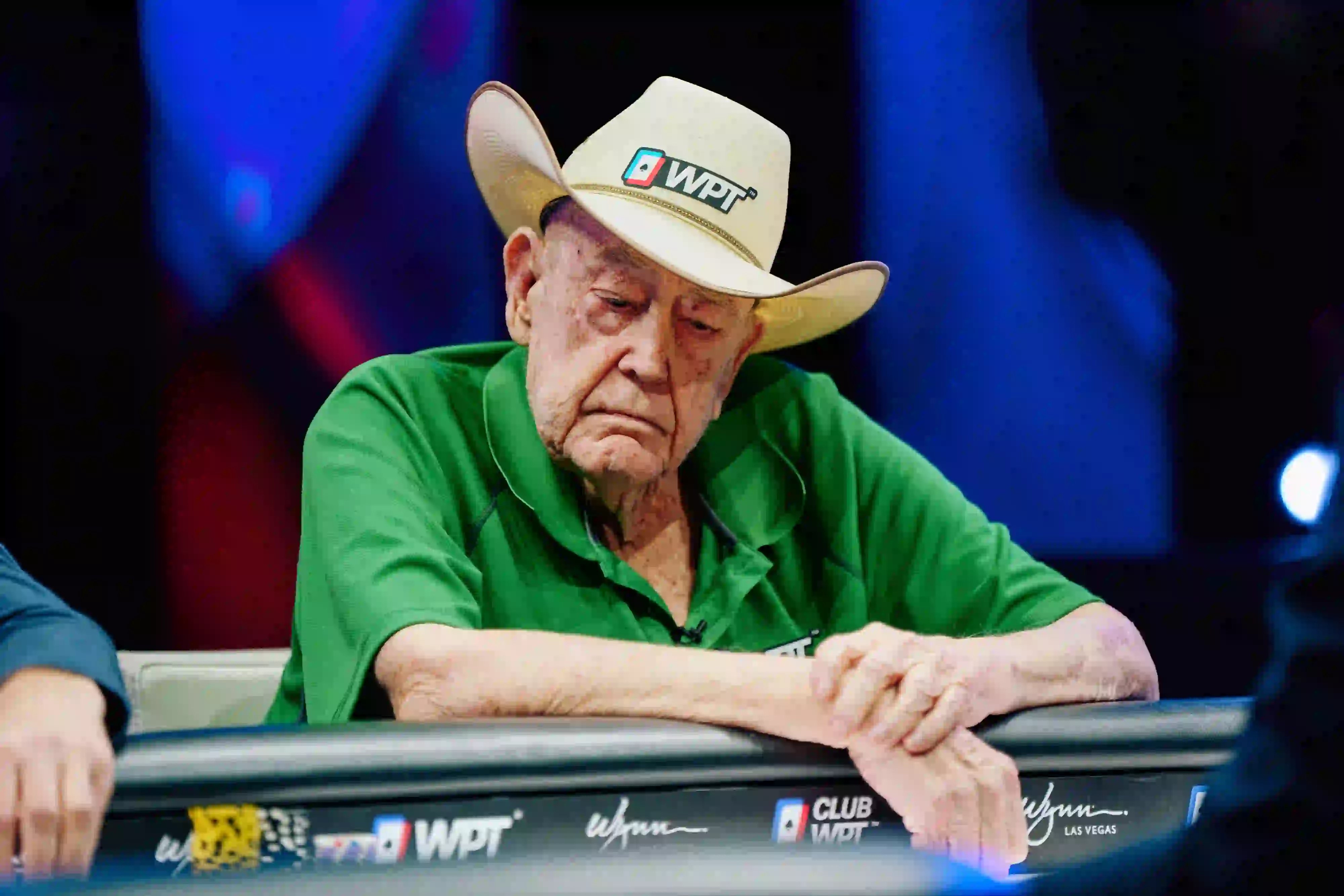 Doyle Brunson in a green WPT® shirt and cowboy hat, sitting at a poker table with a serious expression during a WPT® event.