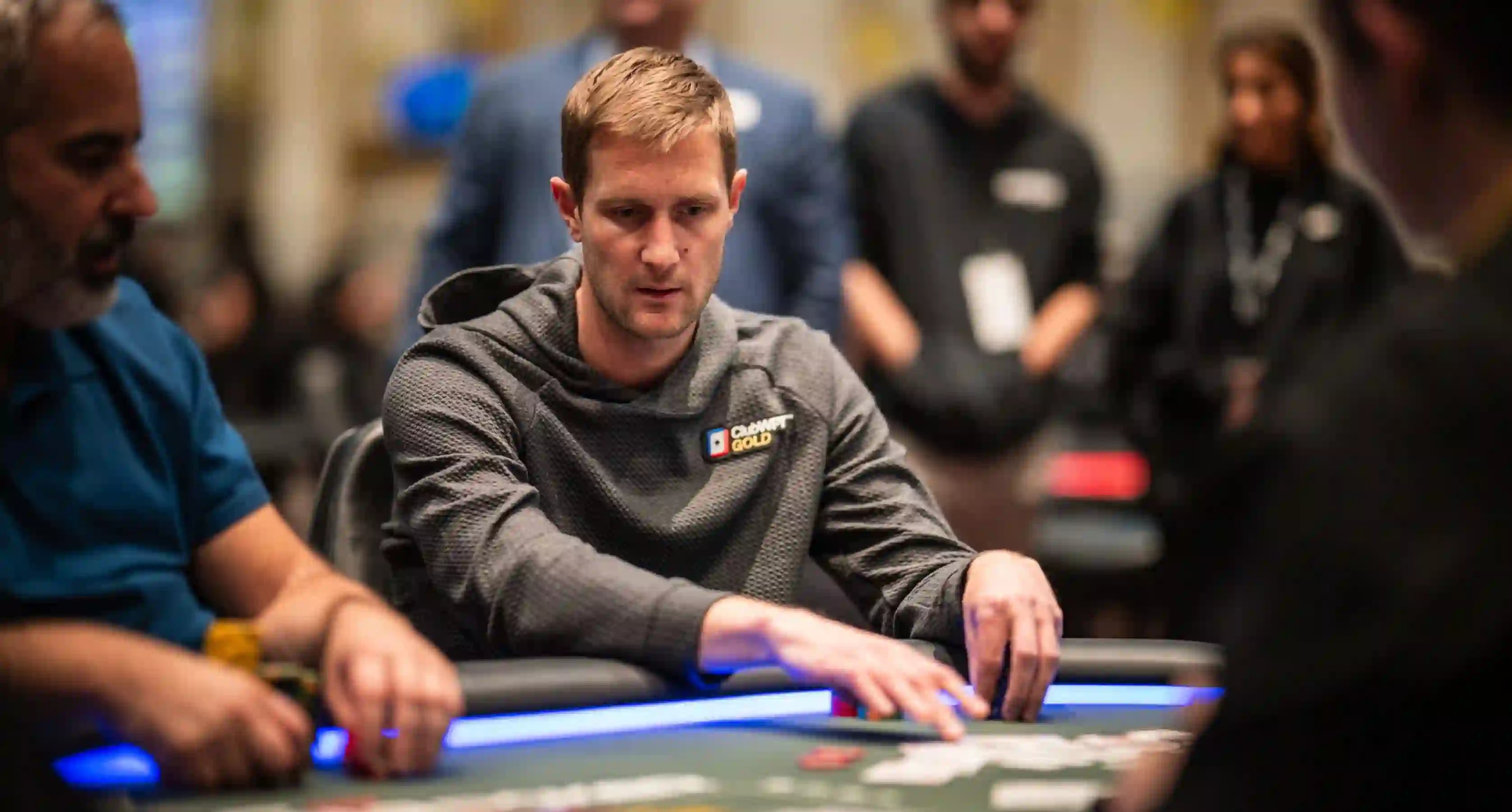 Brad Owen concentrates at the poker table during a live event, reaching forward with chips in front of him.