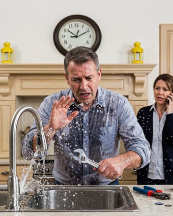 Plumber installing pipes under a residential kitchen sink using tools.