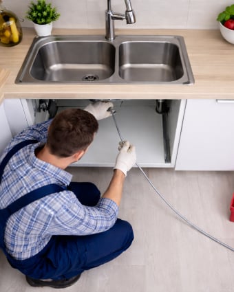 Plumber repairing pipes under a kitchen sink with tools and plumbing parts nearby.